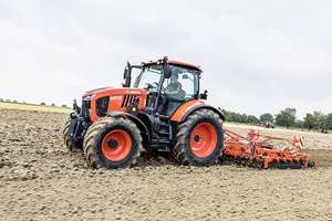 Roter Kubota M6121 Traktor mit Fahrer beim Bodenbearbeiten auf einem Acker mit angehängter Egge.