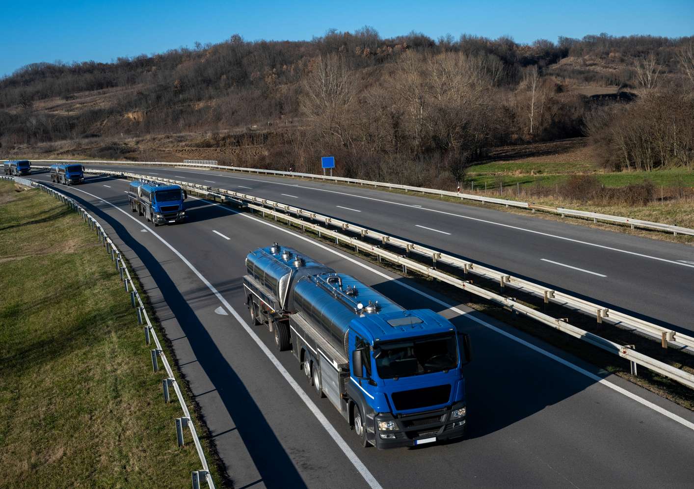 4 blaue LKW mit Milch fahren hintereinander auf der Autobahn in einer herbstlichen Landschaft