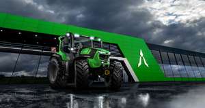 Grüner Deutz-Fahr Traktor mit eingeschalteten Scheinwerfern vor einem modernen grünen Gebäude bei bewölktem Himmel.
