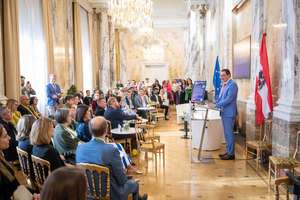 Totschnig hält eine Rede in einem Marmorsaal mit Publikum. Europäische und österreichische Flaggen im Hintergrund.