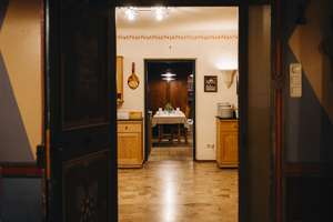 Blick durch eine offene Tür in eine warme, gemütliche Küche mit Holzmöbeln und einem gedeckten Esstisch im Hintergrund.