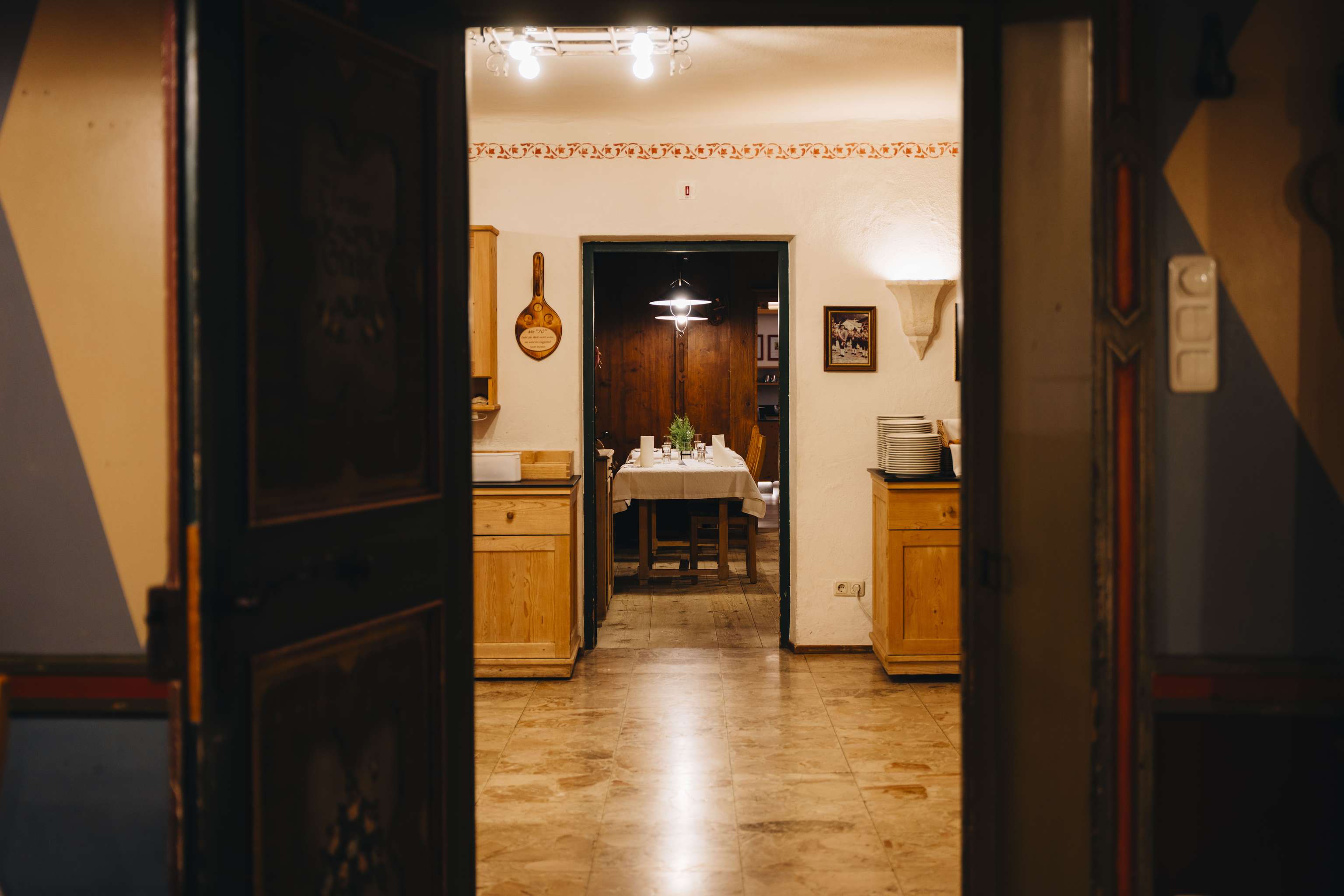 Blick durch eine offene Tür in eine warme, gemütliche Küche mit Holzmöbeln und einem gedeckten Esstisch im Hintergrund.