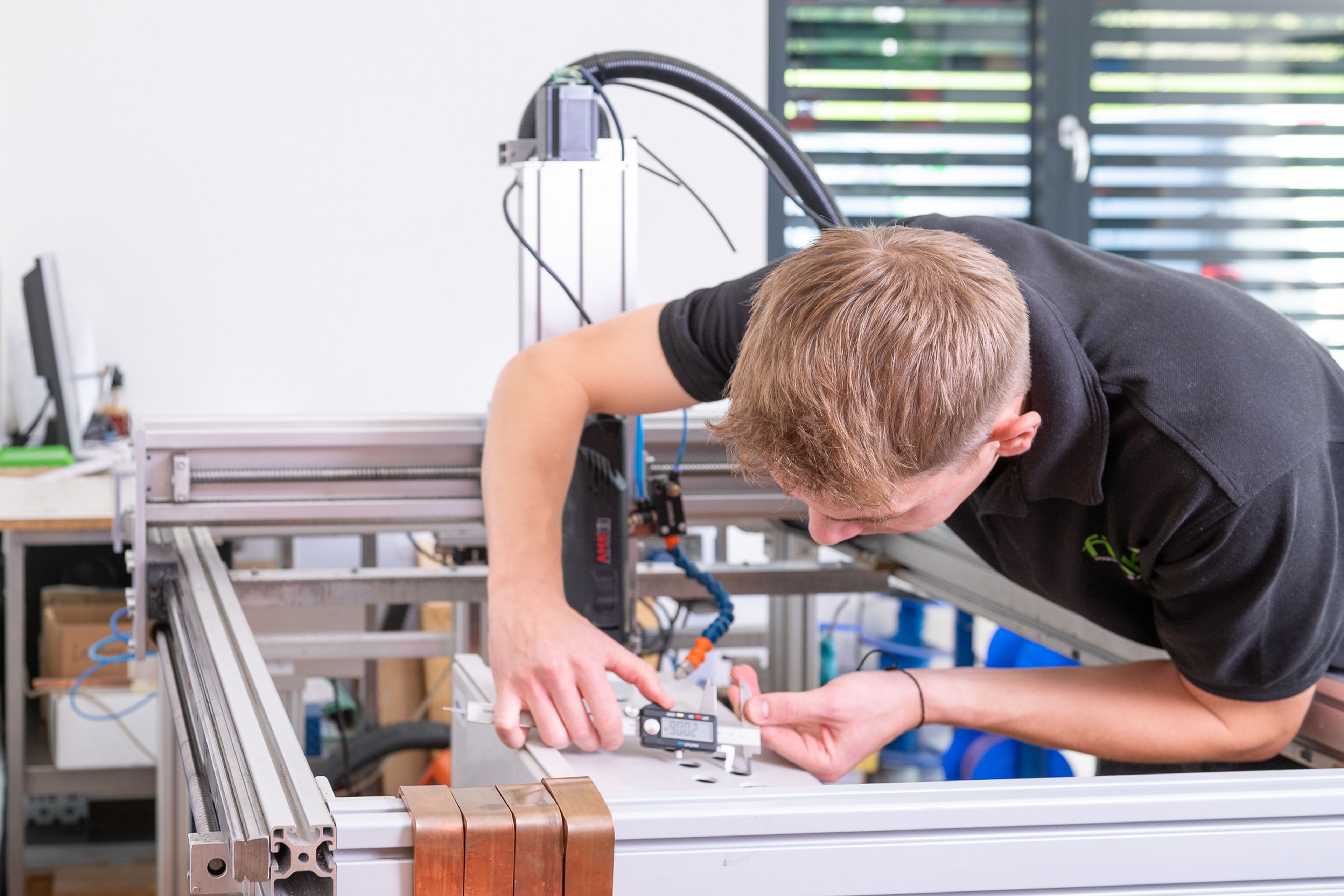 Eine Person, die mit einem Messschieber ein Bauteil an einer CNC-Maschine in einer Werkstatt misst.
