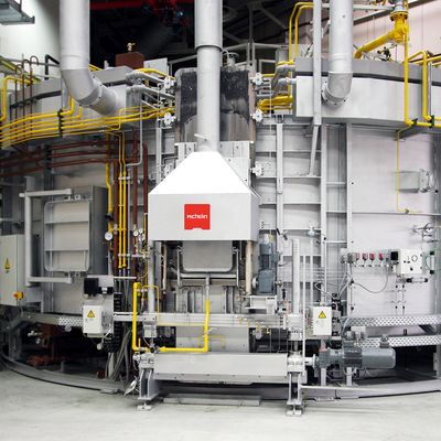 Industrial machine with steel structure, pipes, and yellow safety railings. A red logo is visible on a central white panel.
