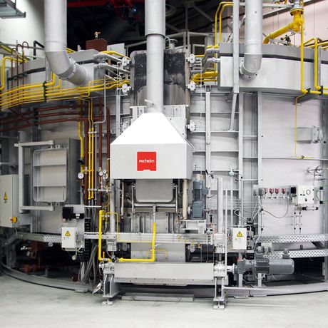 Industrial machine with steel structure, pipes, and yellow safety railings. A red logo is visible on a central white panel.