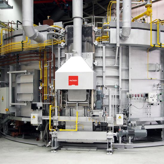 Industrial machine with steel structure, pipes, and yellow safety railings. A red logo is visible on a central white panel.