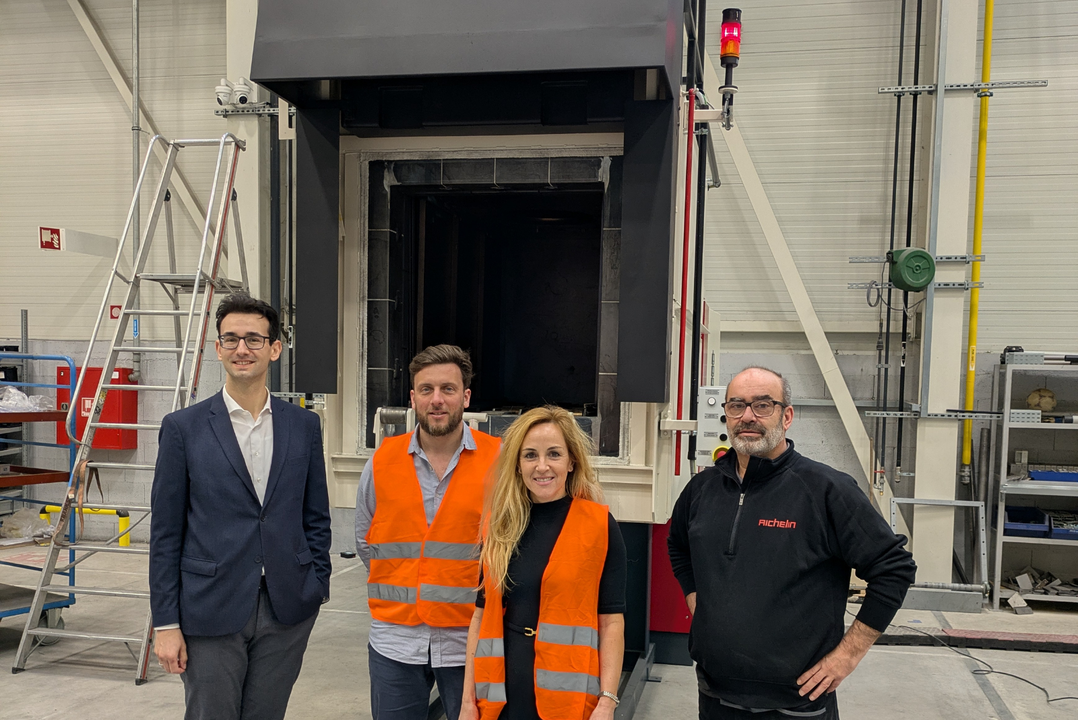 Vier Personen stehen vor einer großen Maschine in einer Fabrikhalle. Zwei tragen orange Sicherheitswesten.
