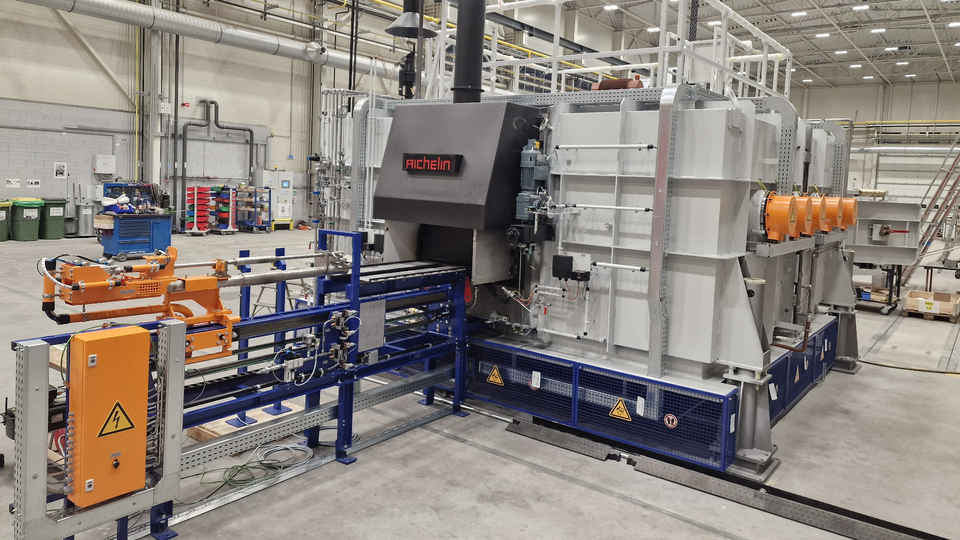 Industrial machinery in a spacious factory with large metal components, orange control boxes, and a robust ventilator system.