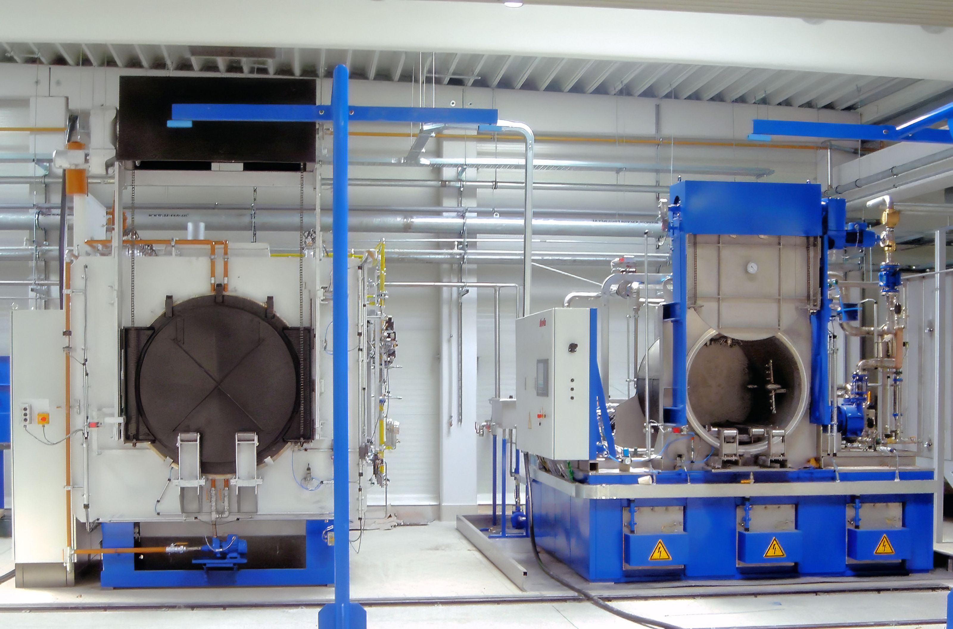 Industrial washer in a factory setting, featuring large metal equipment and various pipes, with a focus on a blue and white color scheme.