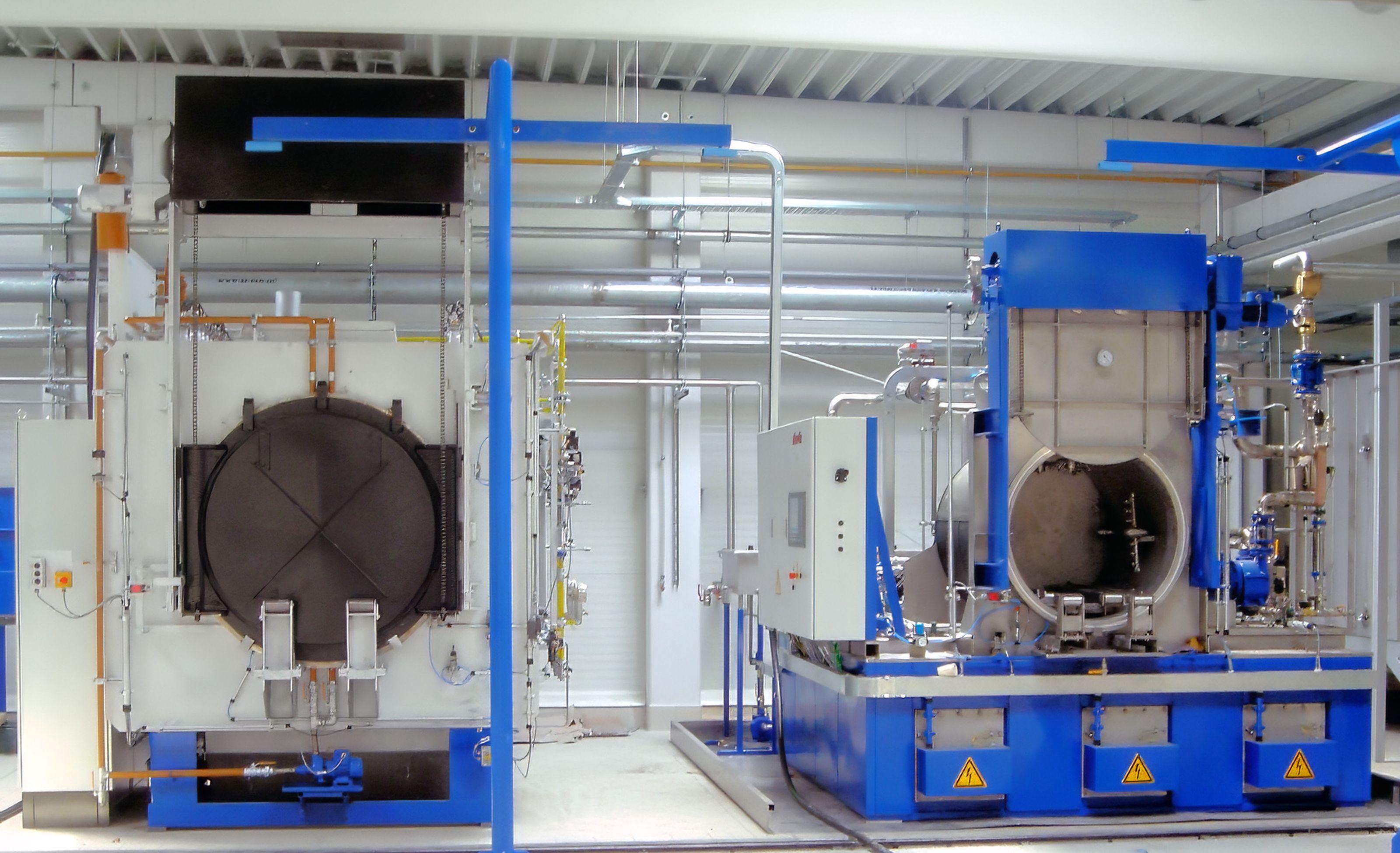 Industrial washer in a factory setting, featuring large metal equipment and various pipes, with a focus on a blue and white color scheme.