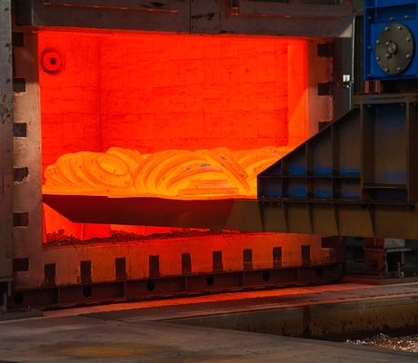 Glowing hot metal coil inside an industrial furnace, with surrounding metal structures and machinery.
