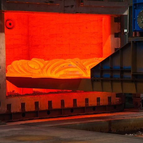 Glowing hot metal coil inside an industrial furnace, with surrounding metal structures and machinery.