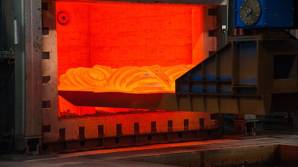 Glowing hot metal coil inside an industrial furnace, with surrounding metal structures and machinery.