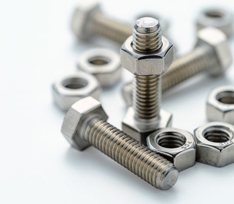 Close-up of several nuts and bolts on a white surface, with two bolts standing upright and others lying scattered around.