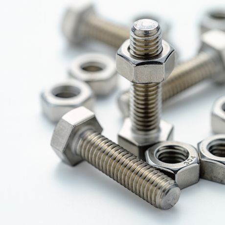 Close-up of several nuts and bolts on a white surface, with two bolts standing upright and others lying scattered around.