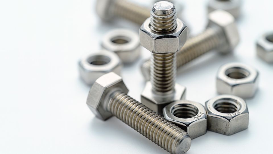 Close-up of several nuts and bolts on a white surface, with two bolts standing upright and others lying scattered around.