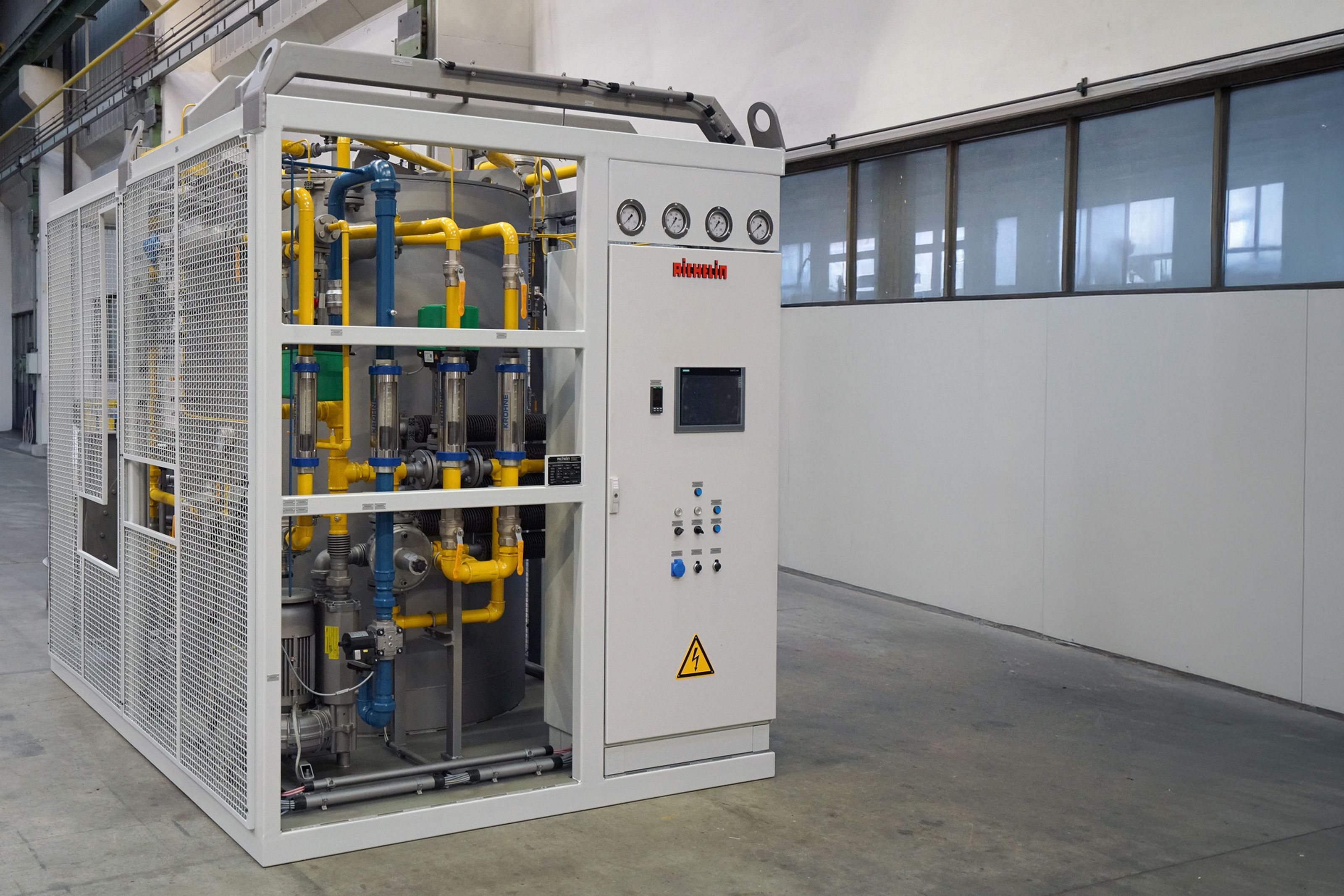 Industrial auxiliary equipment with gauges, pipes, and a control panel inside a metal framework, situated in a spacious, clean facility.