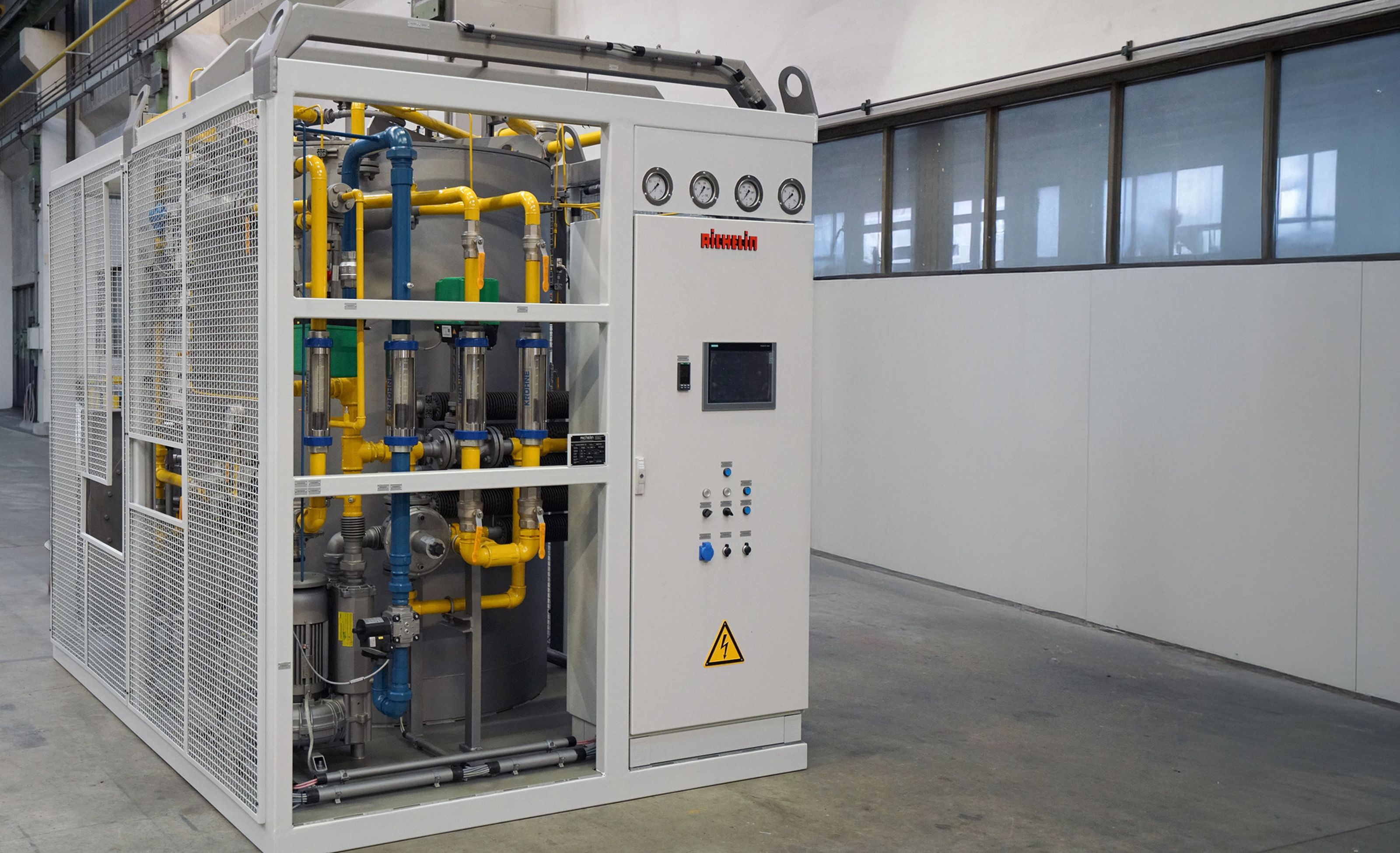 Industrial auxiliary equipment with gauges, pipes, and a control panel inside a metal framework, situated in a spacious, clean facility.