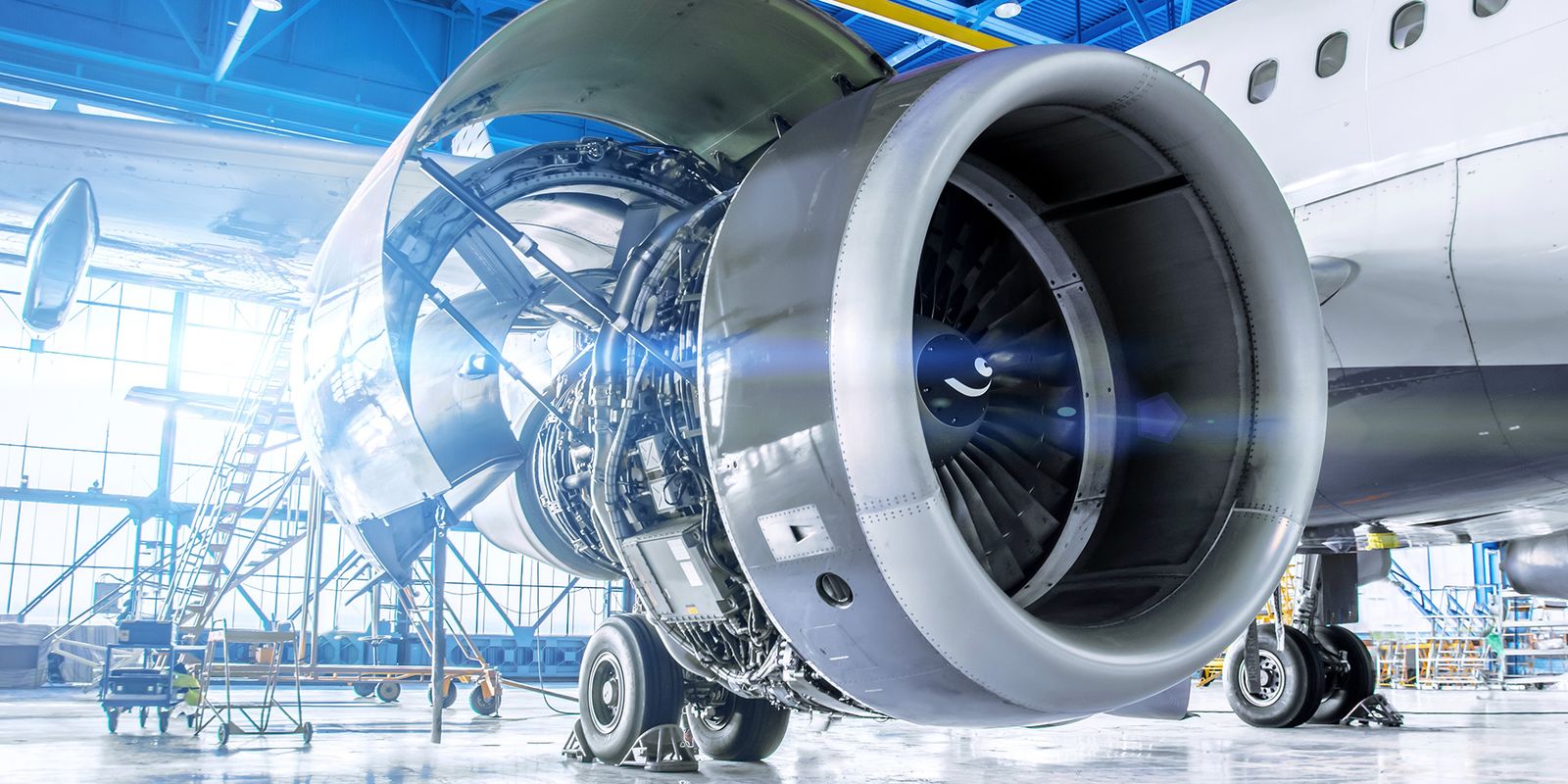 Close-up of a jet engine in a bright airplane hangar, with visible internal components and open cowling, highlighting the engineering details.