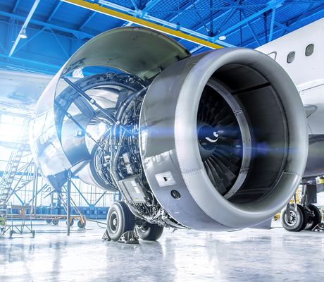Close-up of a jet engine in a bright airplane hangar, with visible internal components and open cowling, highlighting the engineering details.