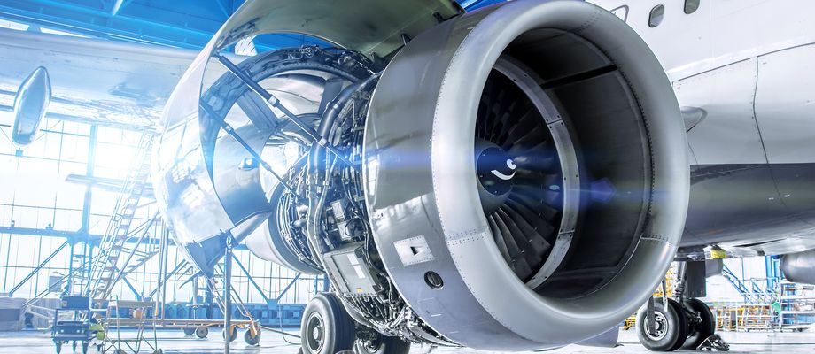 Close-up of a jet engine in a bright airplane hangar, with visible internal components and open cowling, highlighting the engineering details.