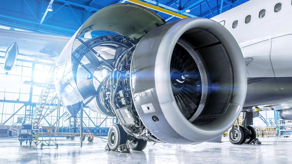 Close-up of a jet engine in a bright airplane hangar, with visible internal components and open cowling, highlighting the engineering details.