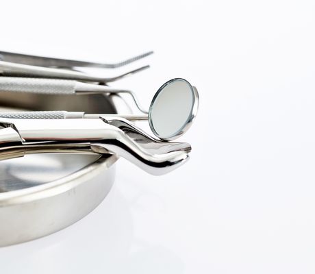 A set of shiny dental tools, including a mirror and tweezers, resting on a metal tray against a white background.