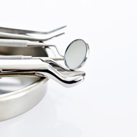 A set of shiny dental tools, including a mirror and tweezers, resting on a metal tray against a white background.