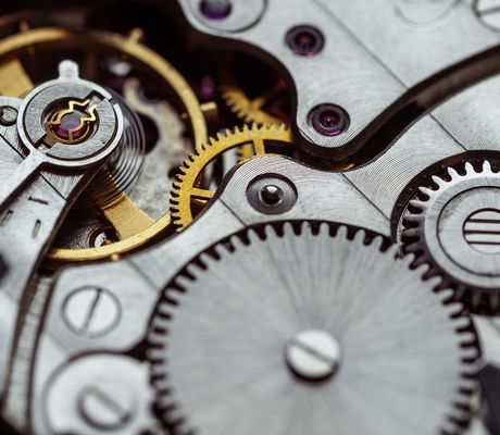Close-up of intricate watch gears and mechanisms in silver and gold, showcasing detailed cogs, wheels, and textures.