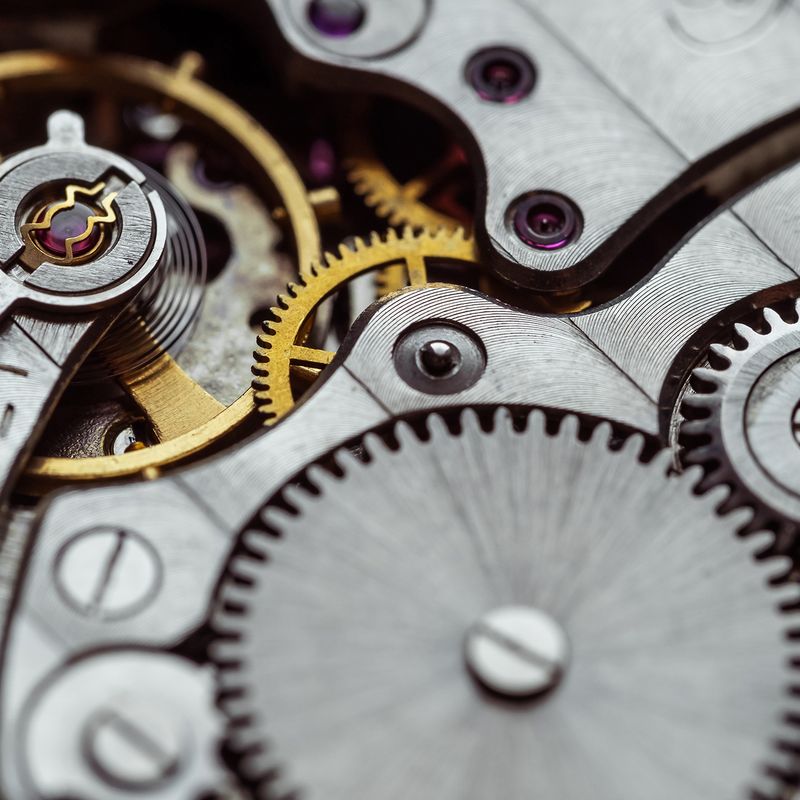 Close-up of intricate watch gears and mechanisms in silver and gold, showcasing detailed cogs, wheels, and textures.
