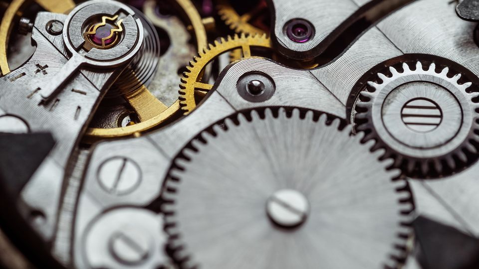 Close-up of intricate watch gears and mechanisms in silver and gold, showcasing detailed cogs, wheels, and textures.
