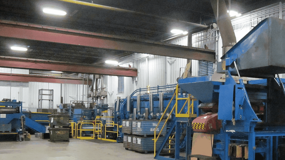 Industrial interior with large blue machinery, metal beams, and bright overhead lighting inside a manufacturing facility.
