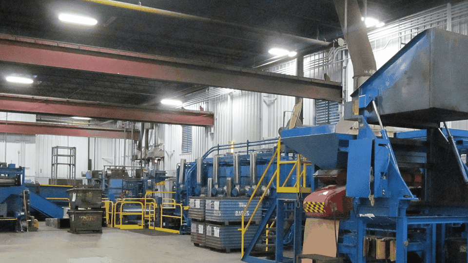 Industrial interior with large blue machinery, metal beams, and bright overhead lighting inside a manufacturing facility.