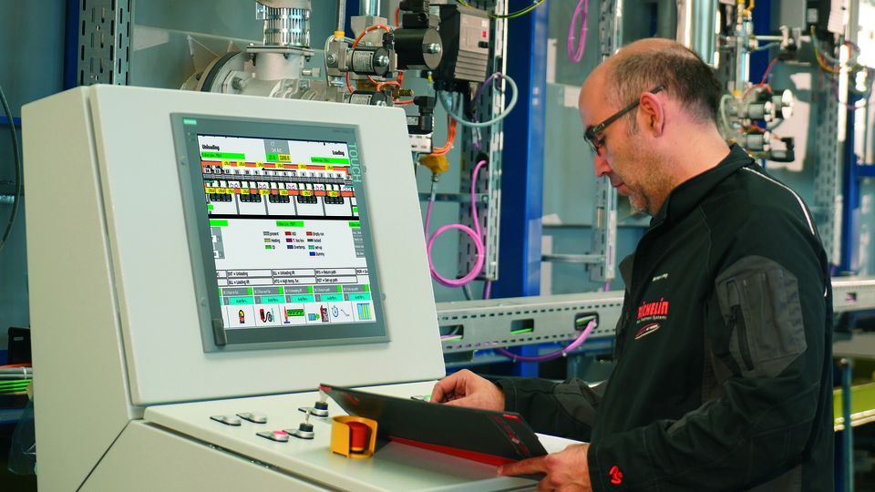 A technician operates a control panel with a digital display in an industrial setting, surrounded by machinery and wiring.