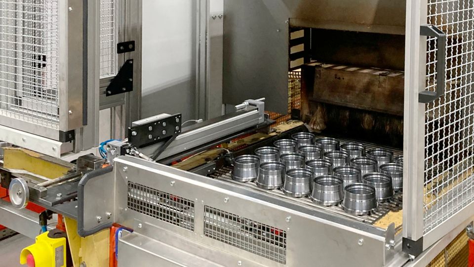 Industrial machine with metal casing and safety barriers containing multiple aluminum containers being processed.