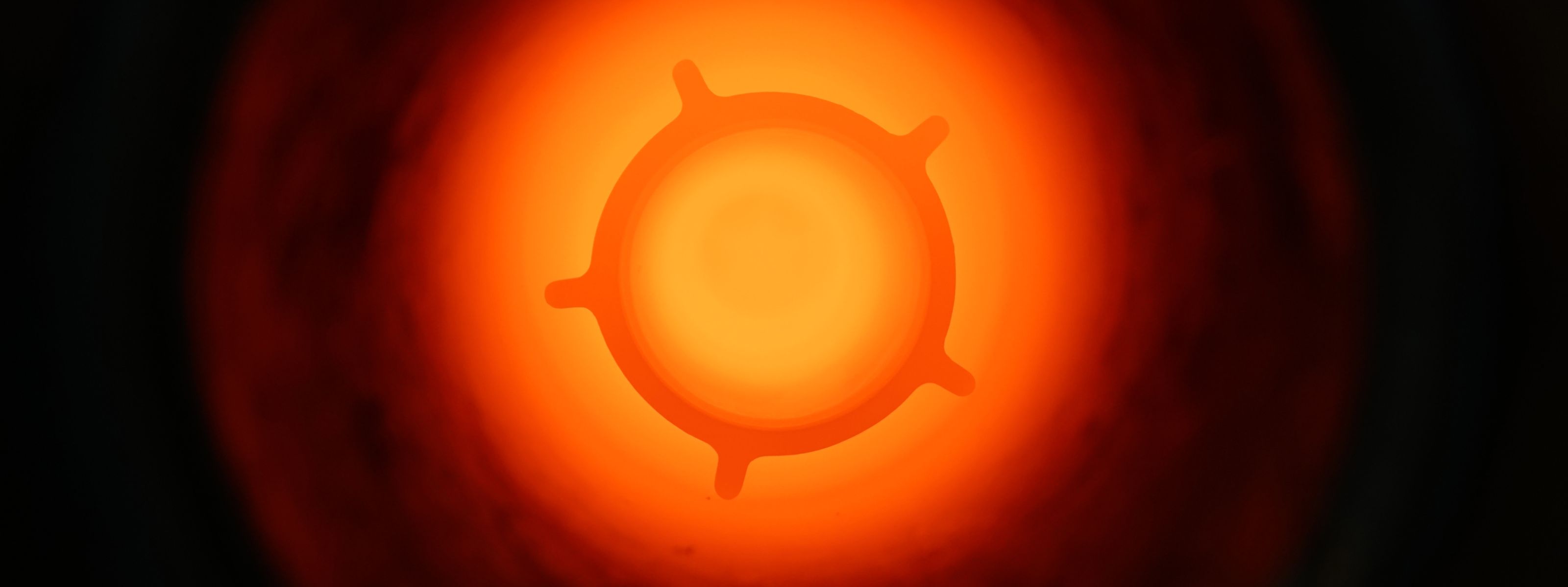 A glowing, abstract shape resembling a cogwheel, centered against a bright orange-red background.
