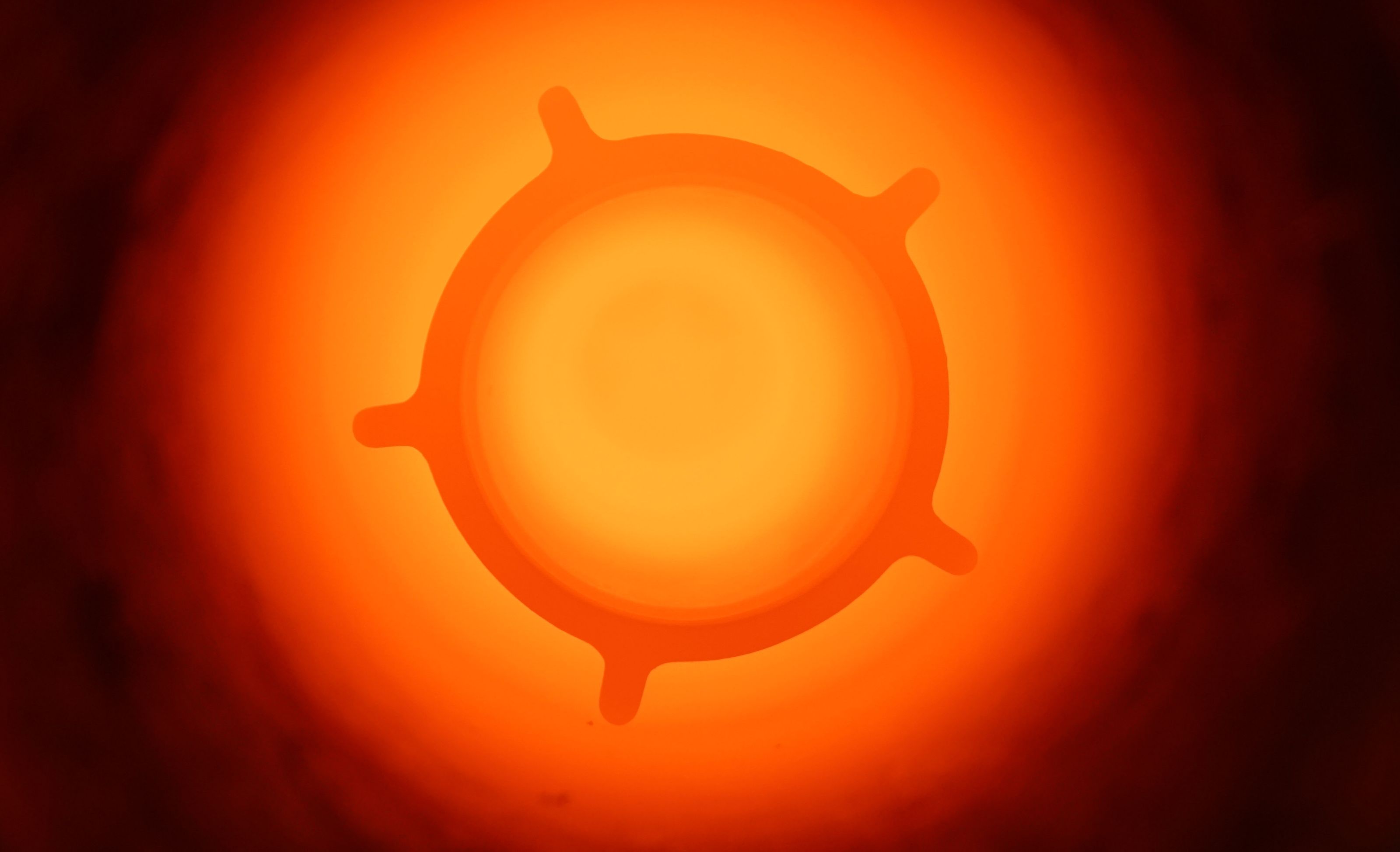 A glowing, abstract shape resembling a cogwheel, centered against a bright orange-red background.