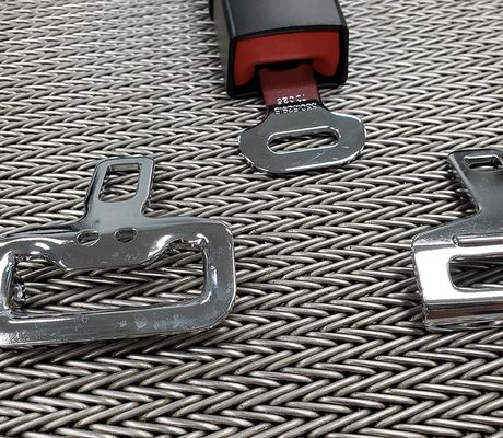 Chrome seatbelt buckles on a textured surface, with one attached to a black strap, showcasing their metallic shine.