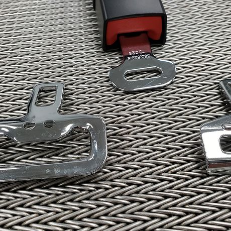 Chrome seatbelt buckles on a textured surface, with one attached to a black strap, showcasing their metallic shine.