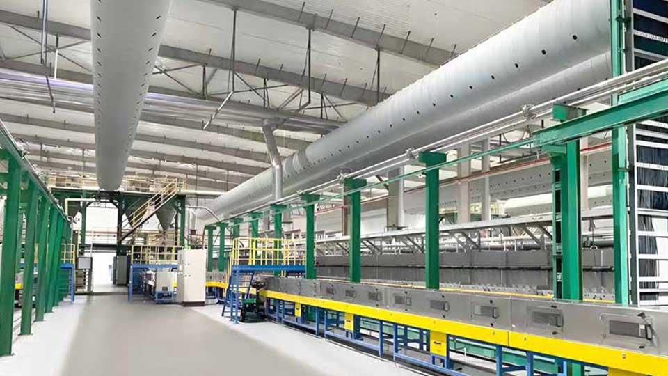 Interior of a modern manufacturing facility with metal structures, conveyors, and large ventilation pipes, brightly lit and spacious.