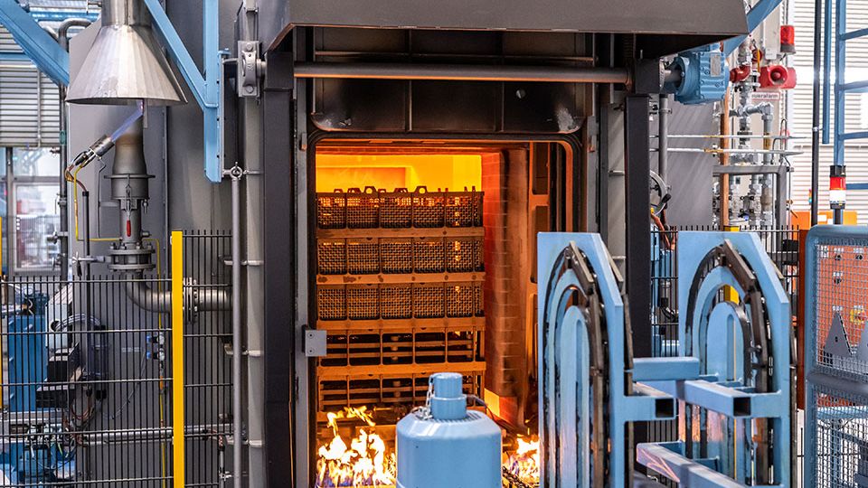 Industrial furnace with bright orange interior heat, metal structures, and machinery, indicating a high-temperature process in progress.