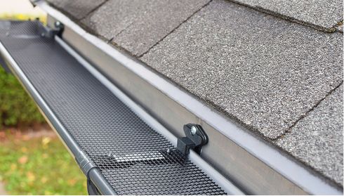 Close-up of a roof with gray shingles and a black mesh gutter guard installed, preventing debris buildup