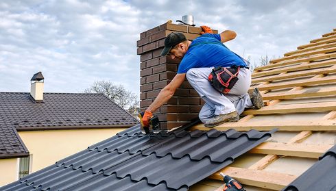 Roofer installing black metal roof panels around chimney