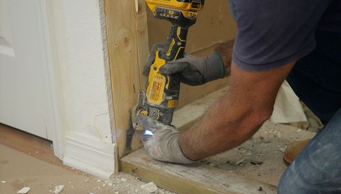 A person uses a yellow power tool to cut a wooden door frame