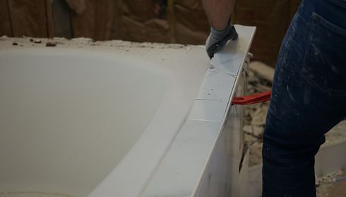 Removing white tiles from a bathtub rim with a red tool