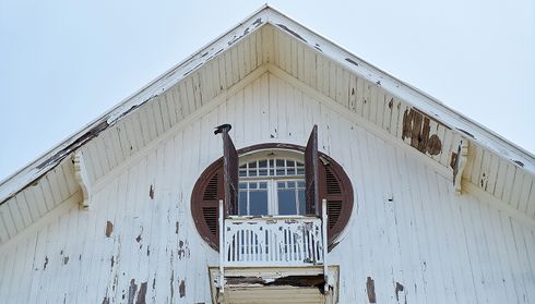 Weathered white siding on a house gable with peeling paint