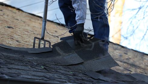 Roofer removing old asphalt shingles before roof replacement
