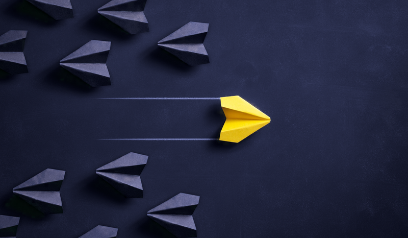 A yellow paper airplane leads a group of black paper airplanes on a dark background, symbolizing leadership and innovation.