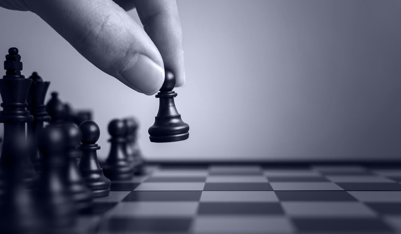 A hand moves a black pawn on a chessboard, with other pieces in the background. The image is in black and white.