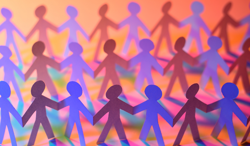 Colorful paper cutouts of people holding hands in rows, casting shadows on a vibrant orange and pink background.
